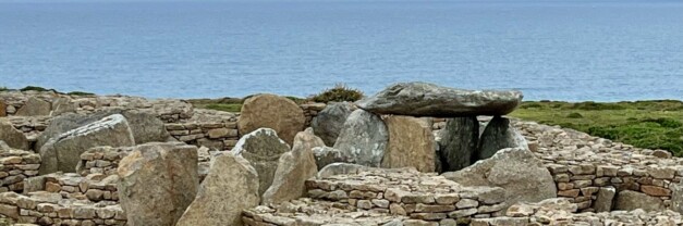 A Neolithic dolmen at Ménez Drégan, Brittany: a large flat capstone resting on upright support stones, set on a hillside of stacked stone walls.